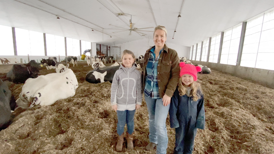 A female dairy farmer with her kids in barn with cows